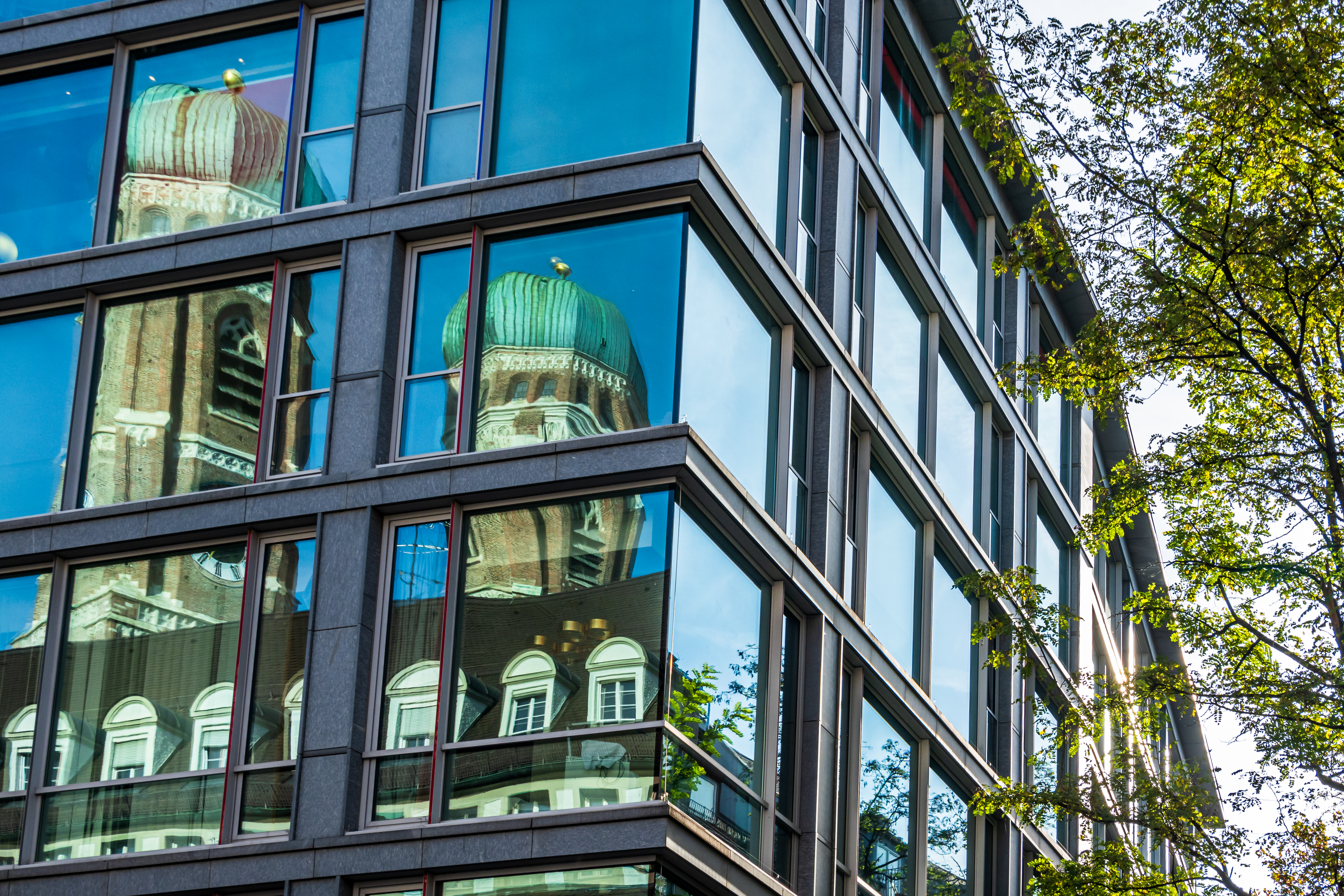 Die Münchner Frauenkirche spiegelt sich in der Glasfassade eines modernen Bürogebäudes
